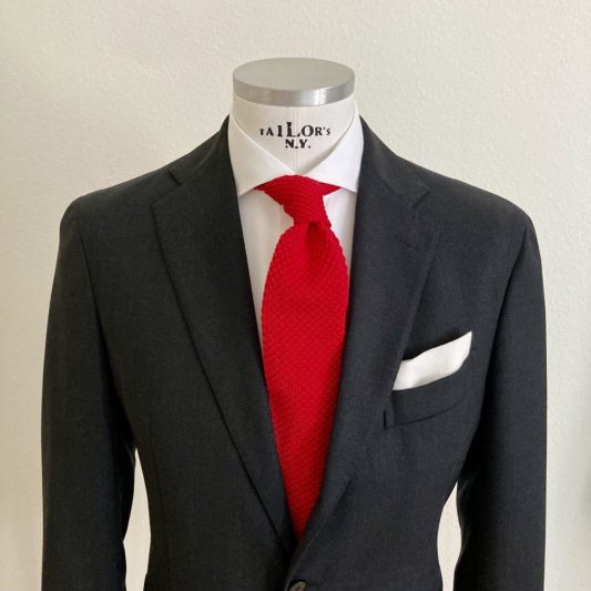 Das Bild zeigt ein Herren Mannequin mit weissem Hochzeitshemd, festlichen Anzug und roten Strickkrawatte sowie weisses Einstecktuch